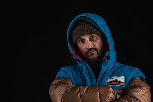 Stylish man in blue hooded winter jacket and beanie against black background.