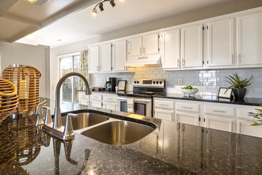 A stylish, contemporary kitchen featuring granite countertops, stainless steel sink, and white cabinets.