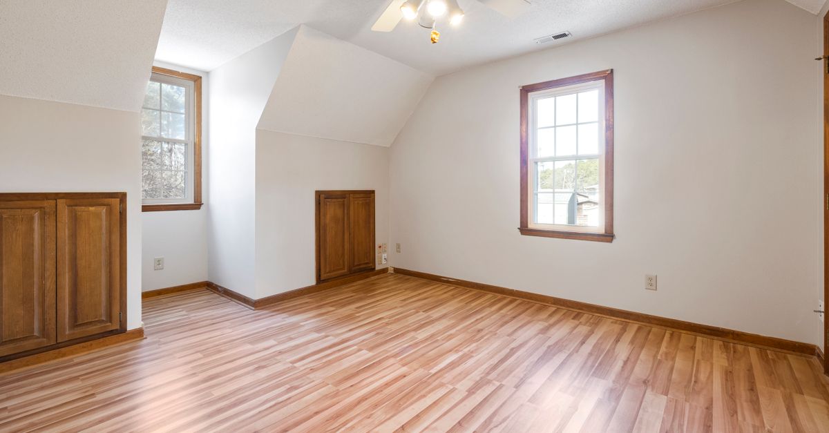 Sunlit empty bedroom featuring wooden floors and ceiling fan, ideal for real estate listings.