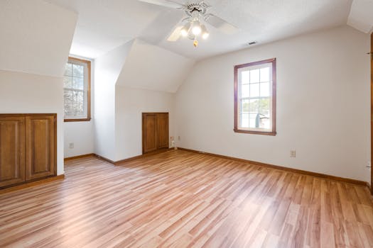 Sunlit empty bedroom featuring wooden floors and ceiling fan, ideal for real estate listings.