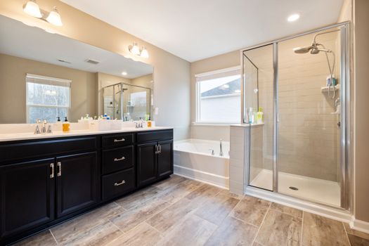 Spacious bathroom featuring a double vanity, bathtub, and glass-enclosed shower with natural light.