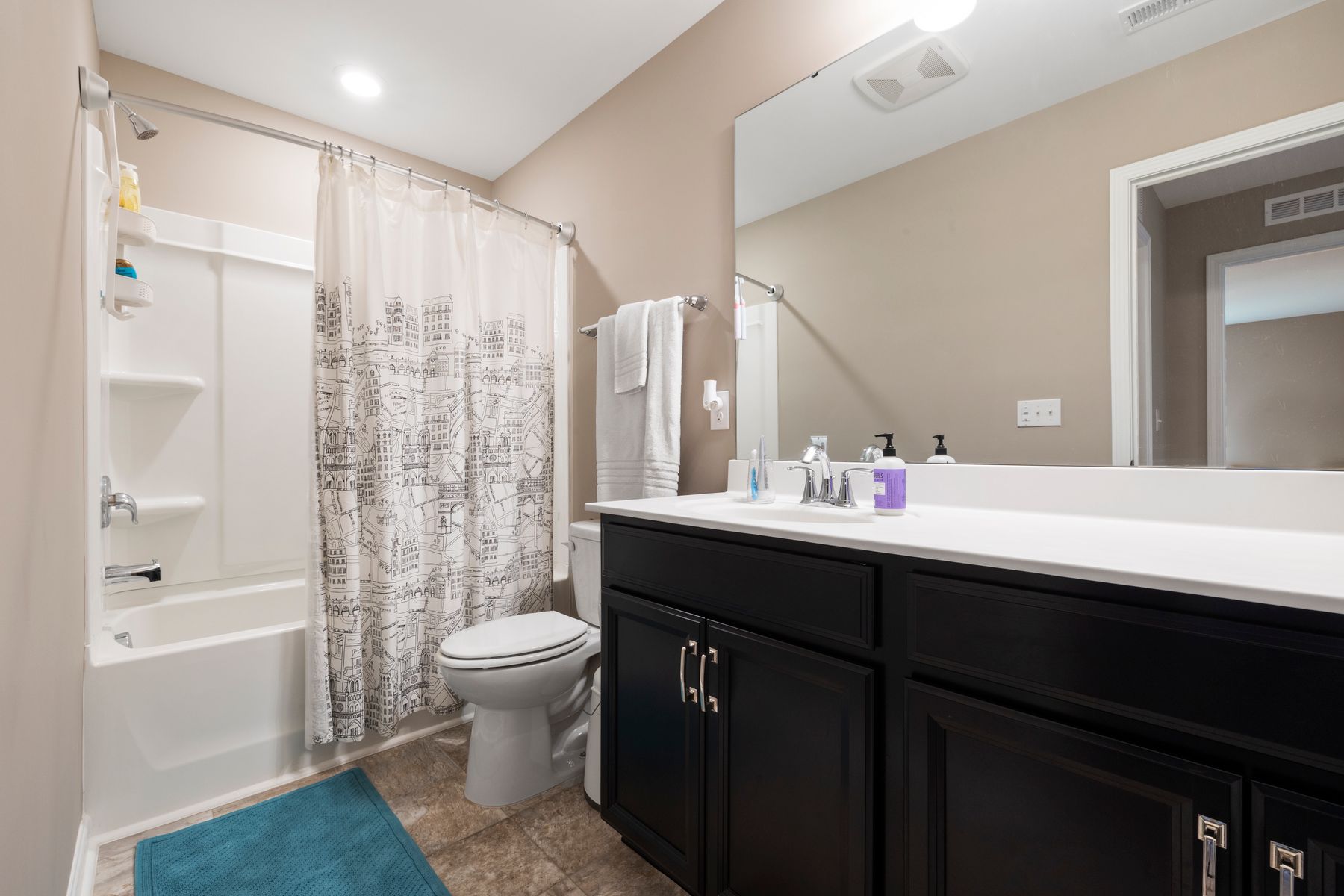 White bathroom with black cabinetry, bathtub and large mirror