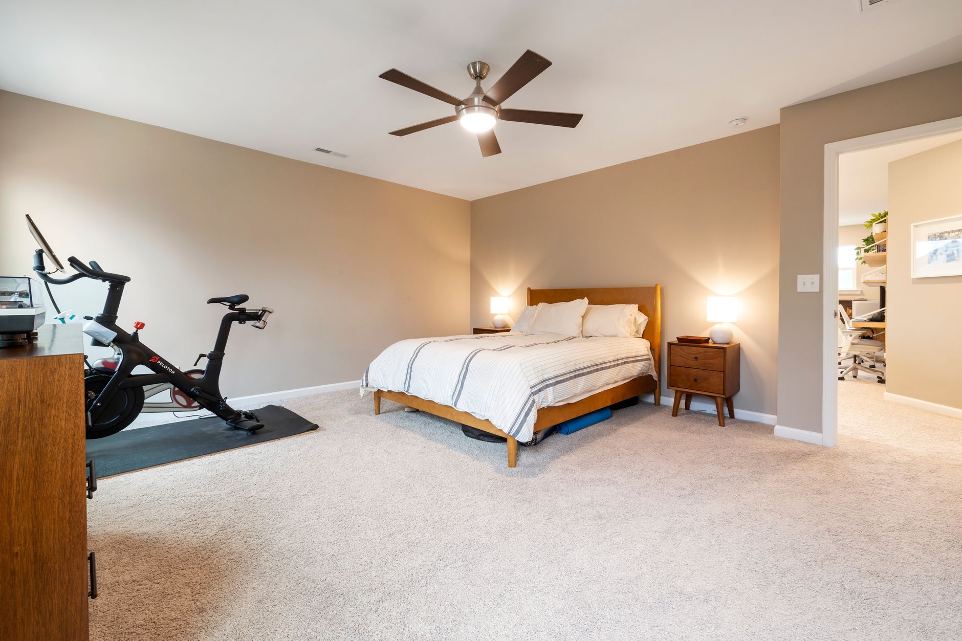 Spacious bedroom featuring a bed, ceiling fan, and stationary bike for a modern lifestyle.
