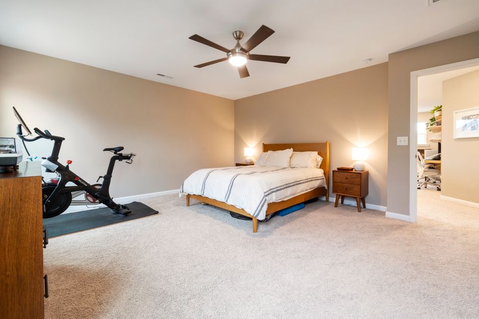 Spacious bedroom featuring a bed, ceiling fan, and stationary bike for a modern lifestyle.