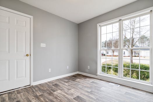 Bright and spacious empty room with wooden flooring and large window, perfect for residential property listings.