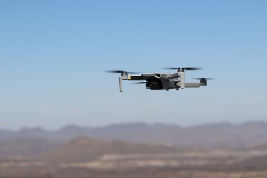 Drone flying over a desert landscape under clear blue skies.