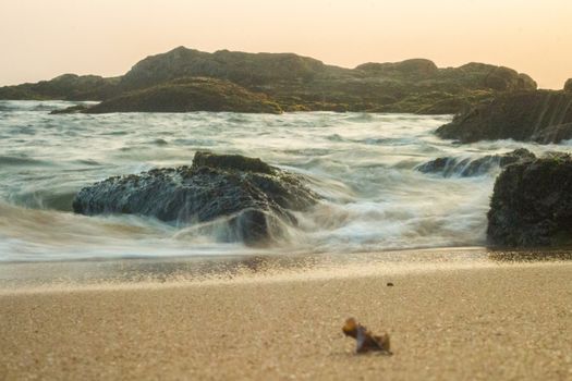 Tranquil beach scene with soft waves, rocky shore, and sunset lighting.