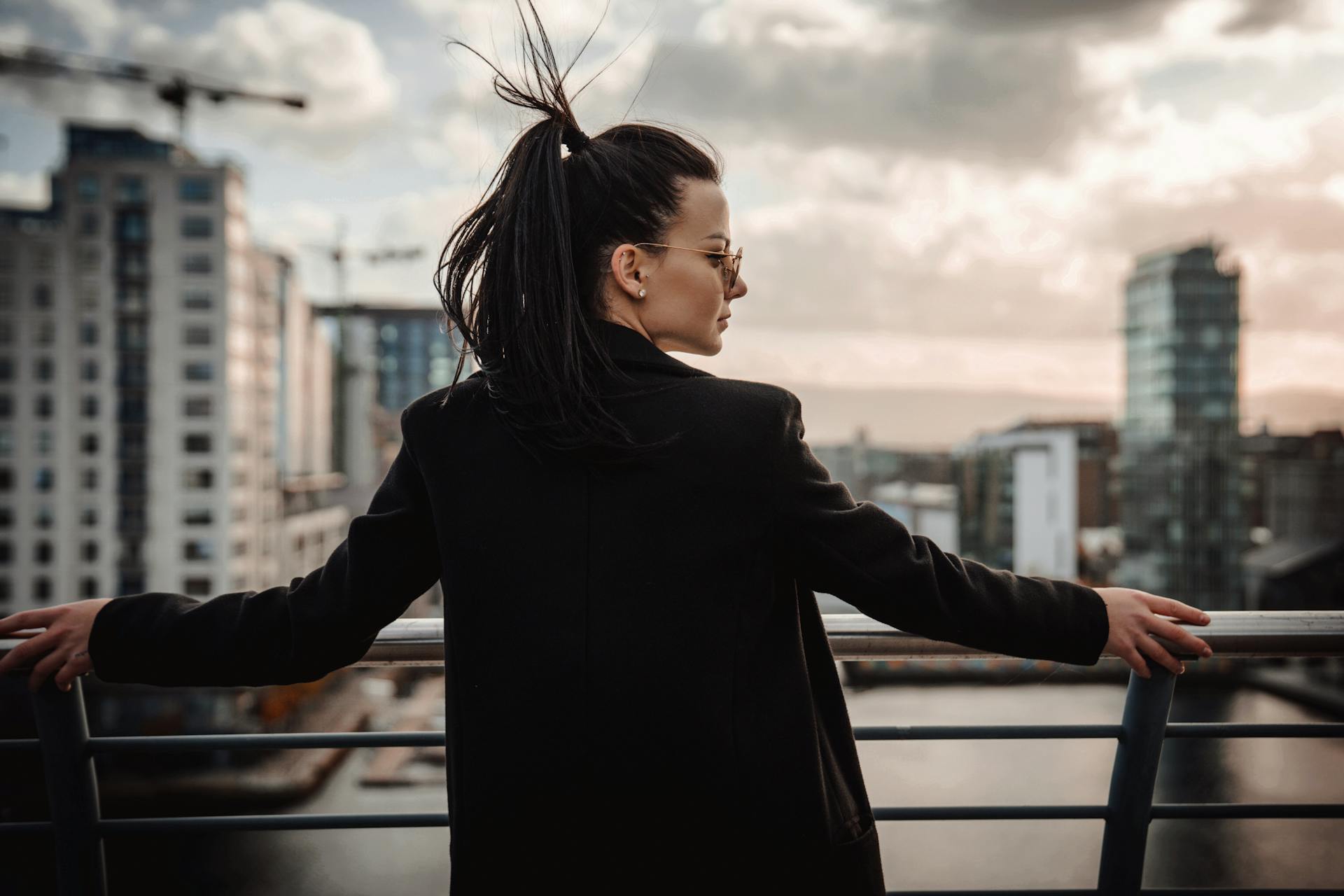 Woman wearing black coat gazing at Dublin skyline from bridge. Modern cityscape in evening light.