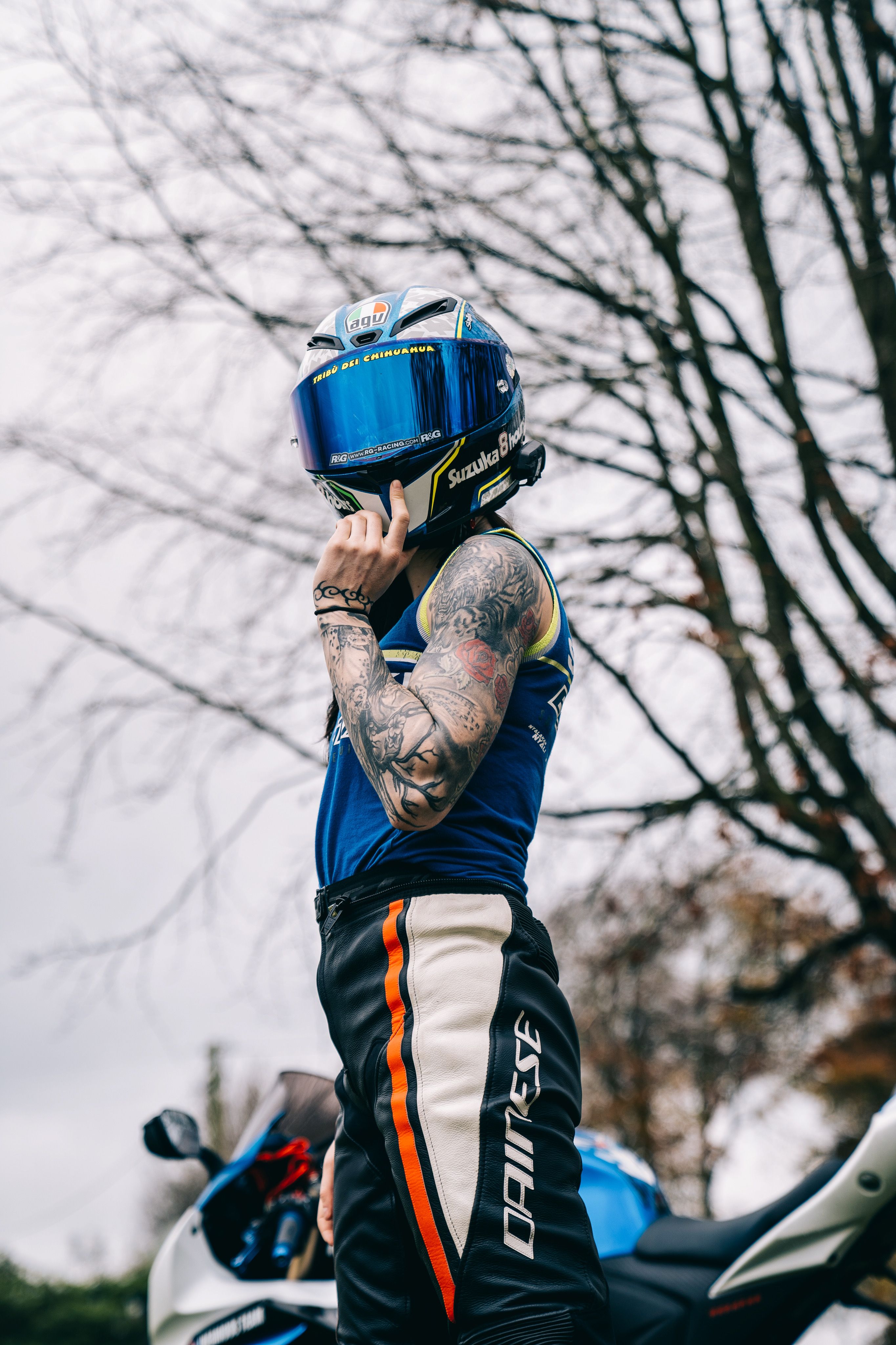 A tattooed motorcyclist poses with a helmet in a Dublin park with winter trees.