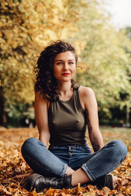 
A Woman Wearing a Tank Top and Denim Pants Sitting on Dried Leaves