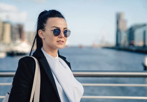 Portrait of a stylish woman in a black blazer and sunglasses by a river in Dublin, Ireland.