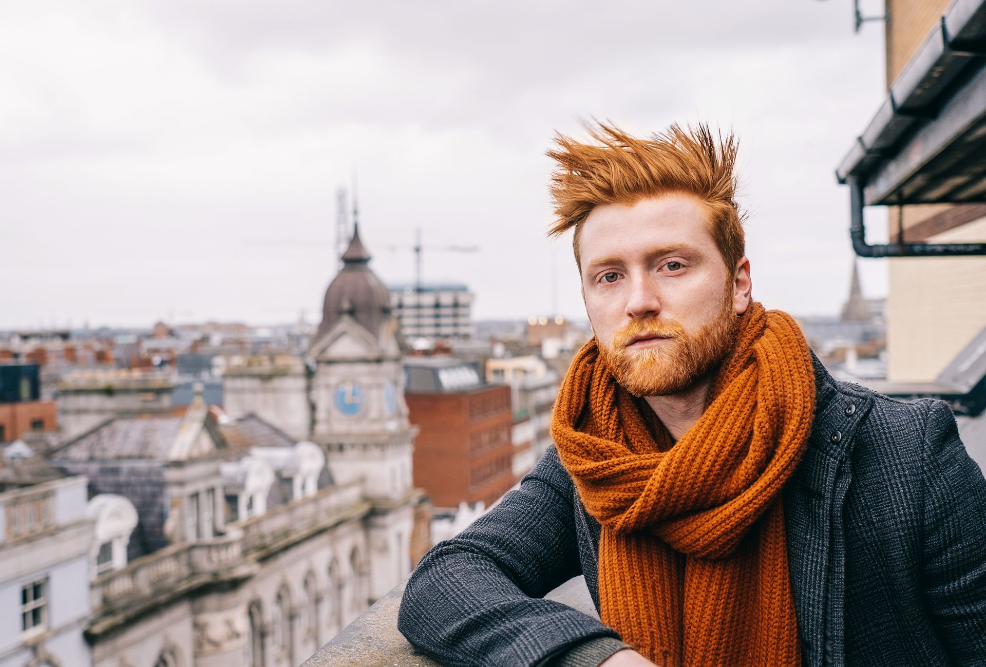 Stylish man with red hair and scarf posing on a Dublin rooftop, capturing urban style.