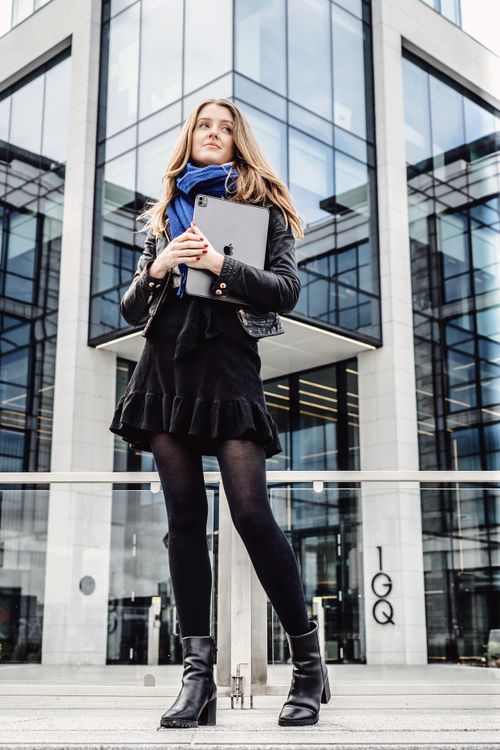 Free Fashionable woman holding a tablet and posing confidently in front of a modern building. Stock Photo