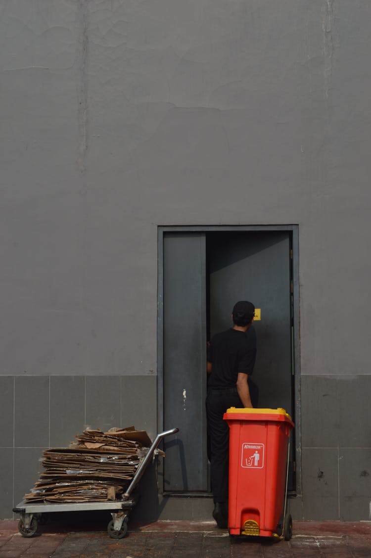 A Person Going Inside The Door While Holding A Trash Bin Cart