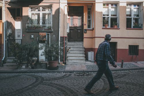 Free A man walks past a door with a cat on steps in a picturesque urban setting. Stock Photo