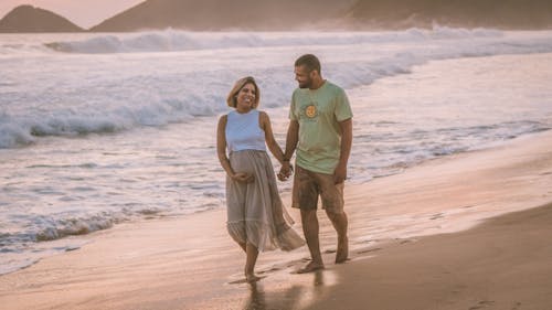 Free Pregnant Woman with her Husband walking on a Shore  Stock Photo