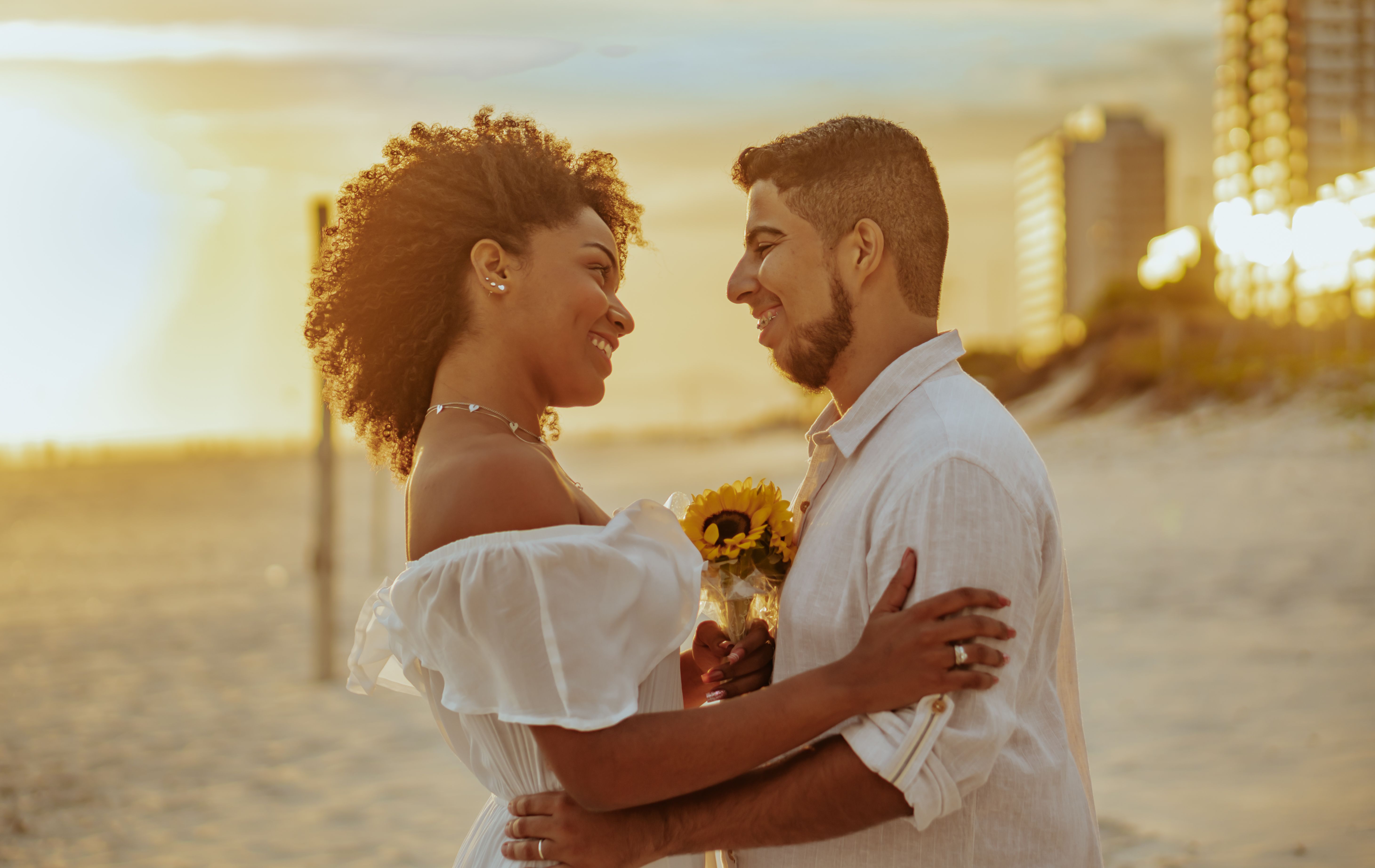 A joyful couple embraces with sunflowers during a sunset beach getaway in Brazil.