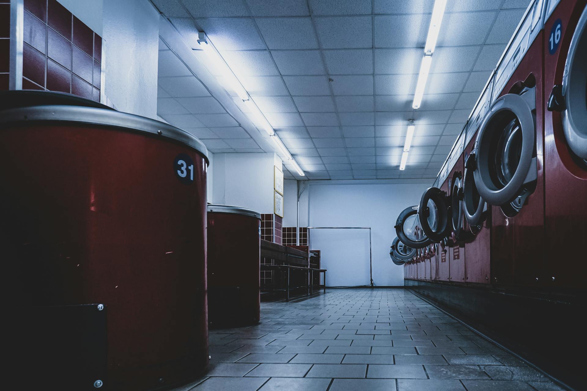 Interior view of a contemporary laundromat featuring red washing machines under fluorescent lights.