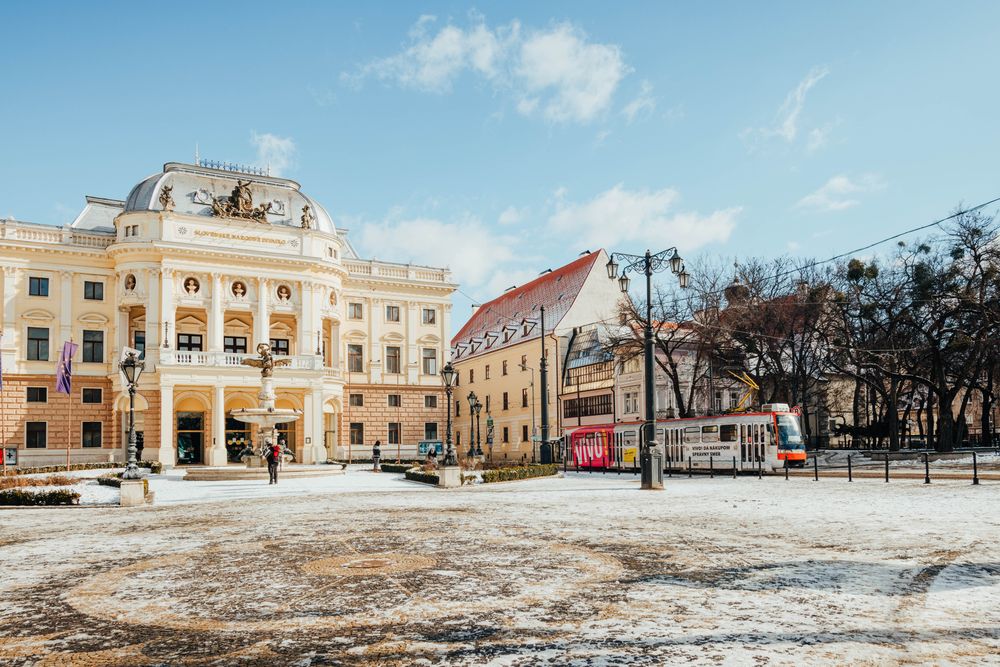 Clădirea Teatrului Național Slovac din Bratislava iarna, cu un tramvai roșu trecând prin fața ei