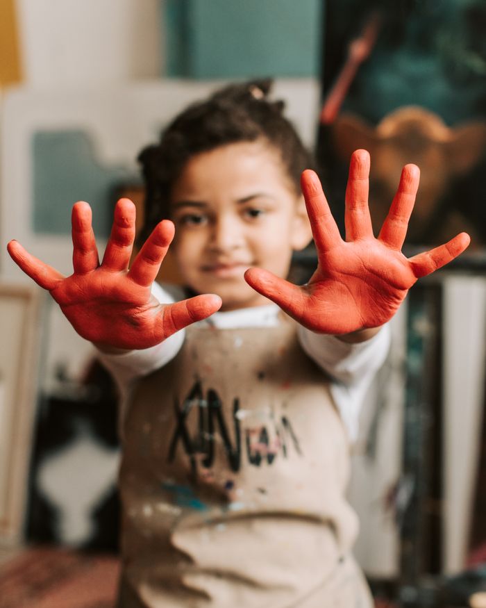 A smiling child holding up hands covered in red paint