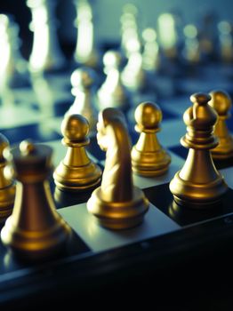 Elegant golden chess pieces set up on a chessboard with a blurred background.
