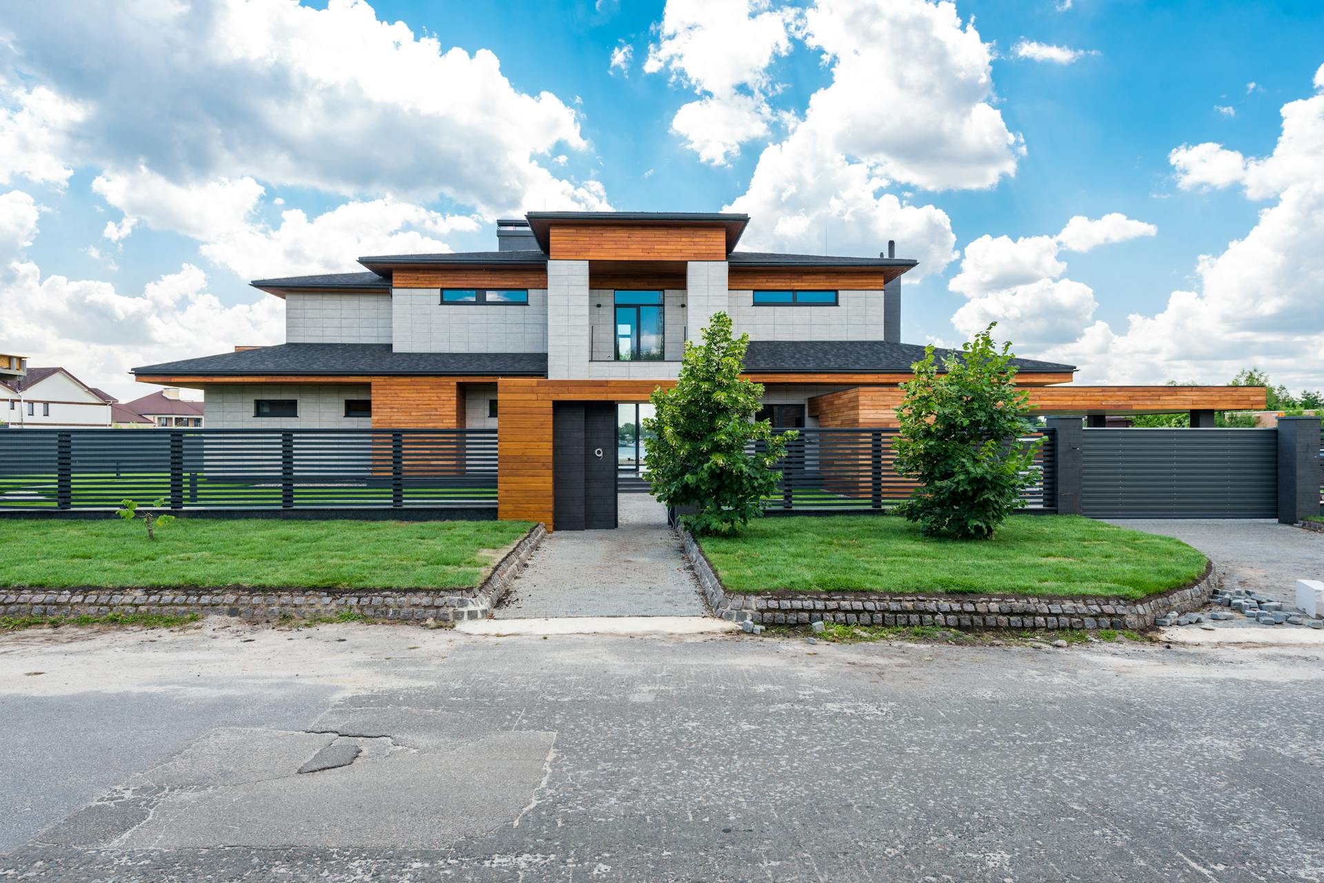 Facade of contemporary luxury villa building with lawn and green trees under blue sky with clouds