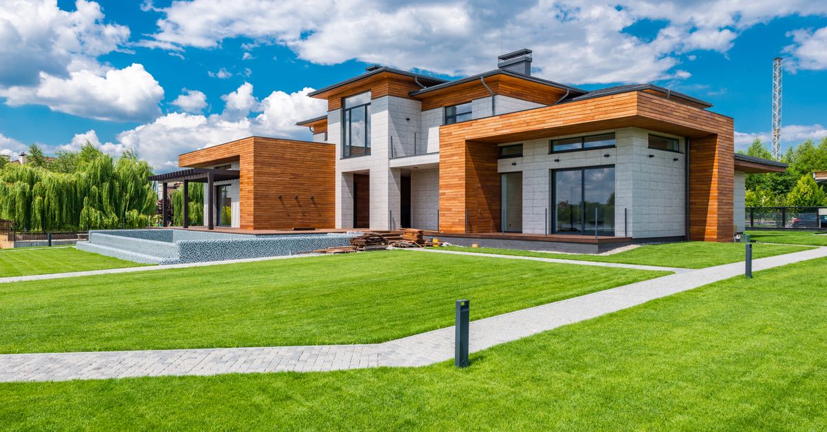 Exterior of contemporary residential house with green yard and paths near forest in summer