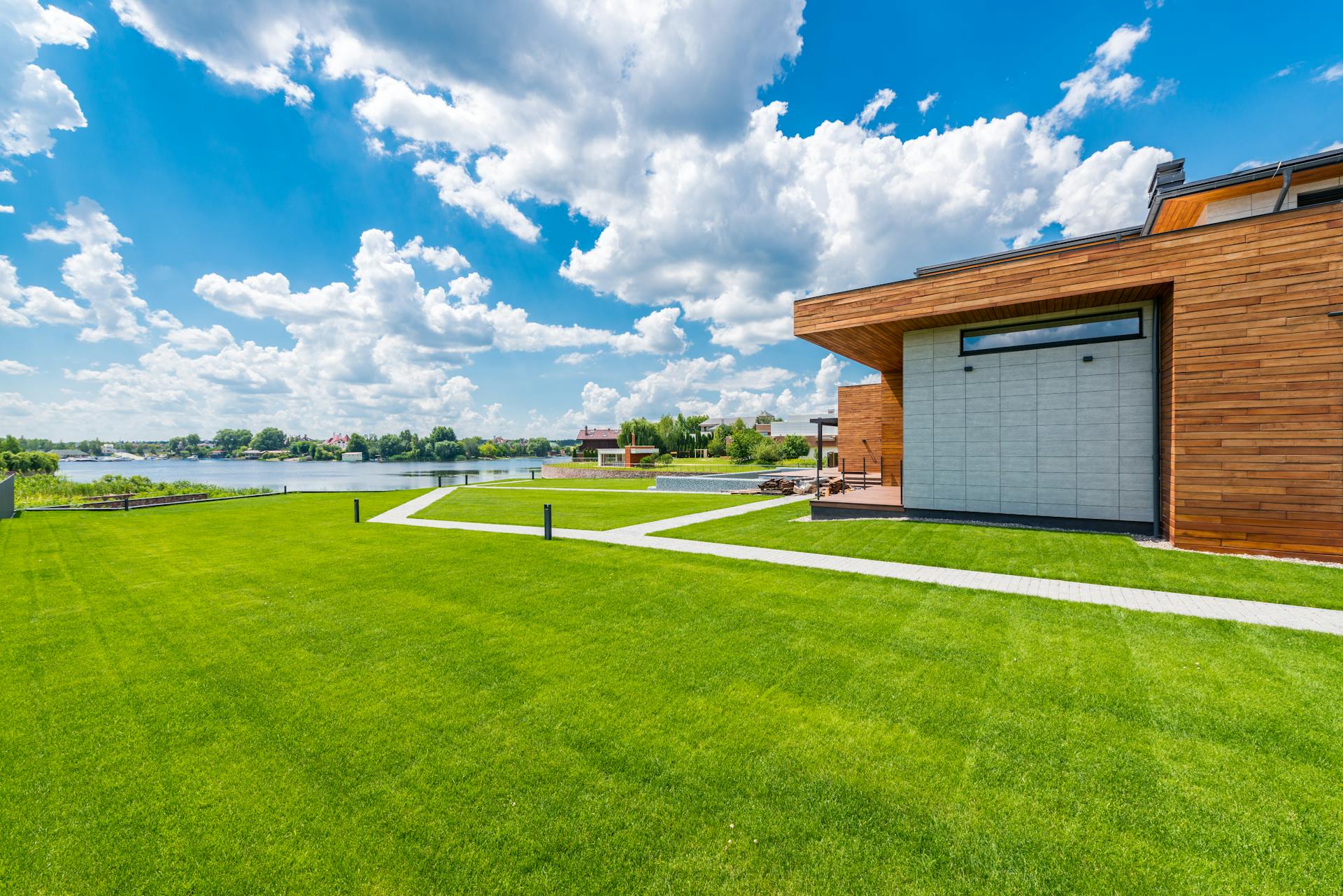 A contemporary home by the lake with vibrant green lawns under a bright blue sky.