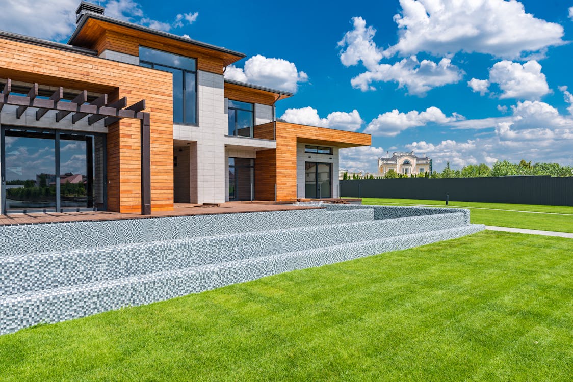 Free Exterior of contemporary residential house with panoramic windows glass doors and green lawn in yard on sunny day against blue sky with white clouds Stock Photo