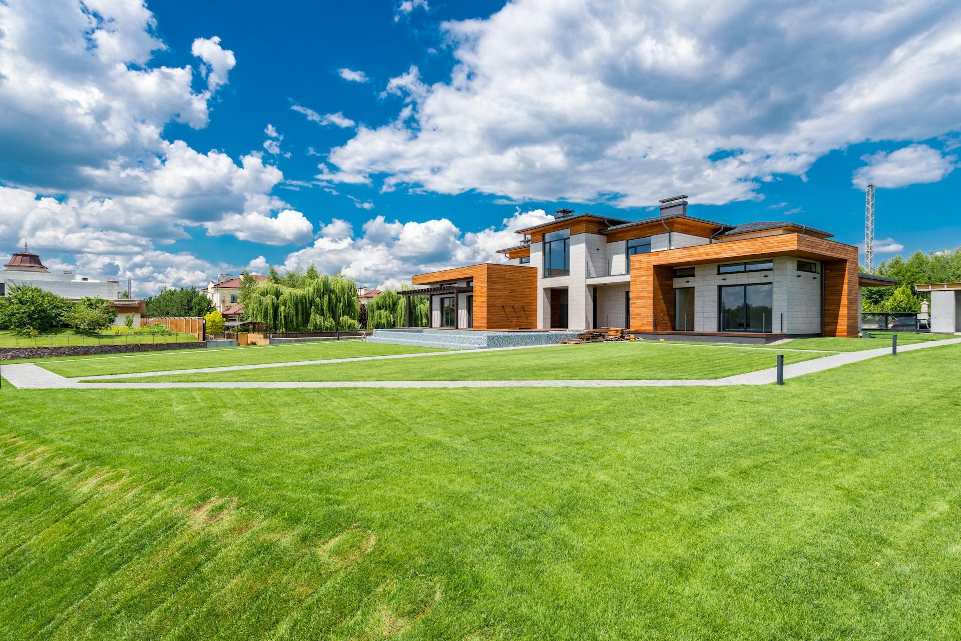 Exterior of modern residential house with wooden walls and green grass growing in yard against blue sky with white clouds