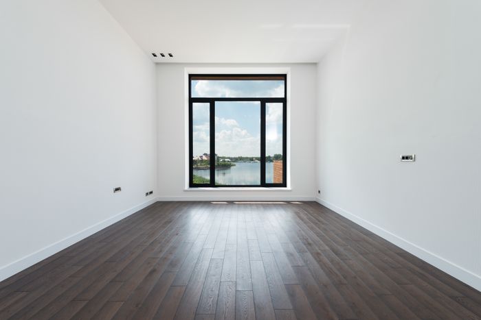 Fertig gestrichener heller Raum mit dunklem Dielenboden und bodentiefem Fenster