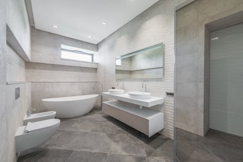 Interior of contemporary bathroom with white ceramic sink and bathtub with faucet on cabinet near mirror