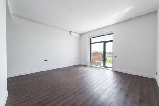 Bright and spacious modern room with a dark wooden floor and large window offering outdoor view.