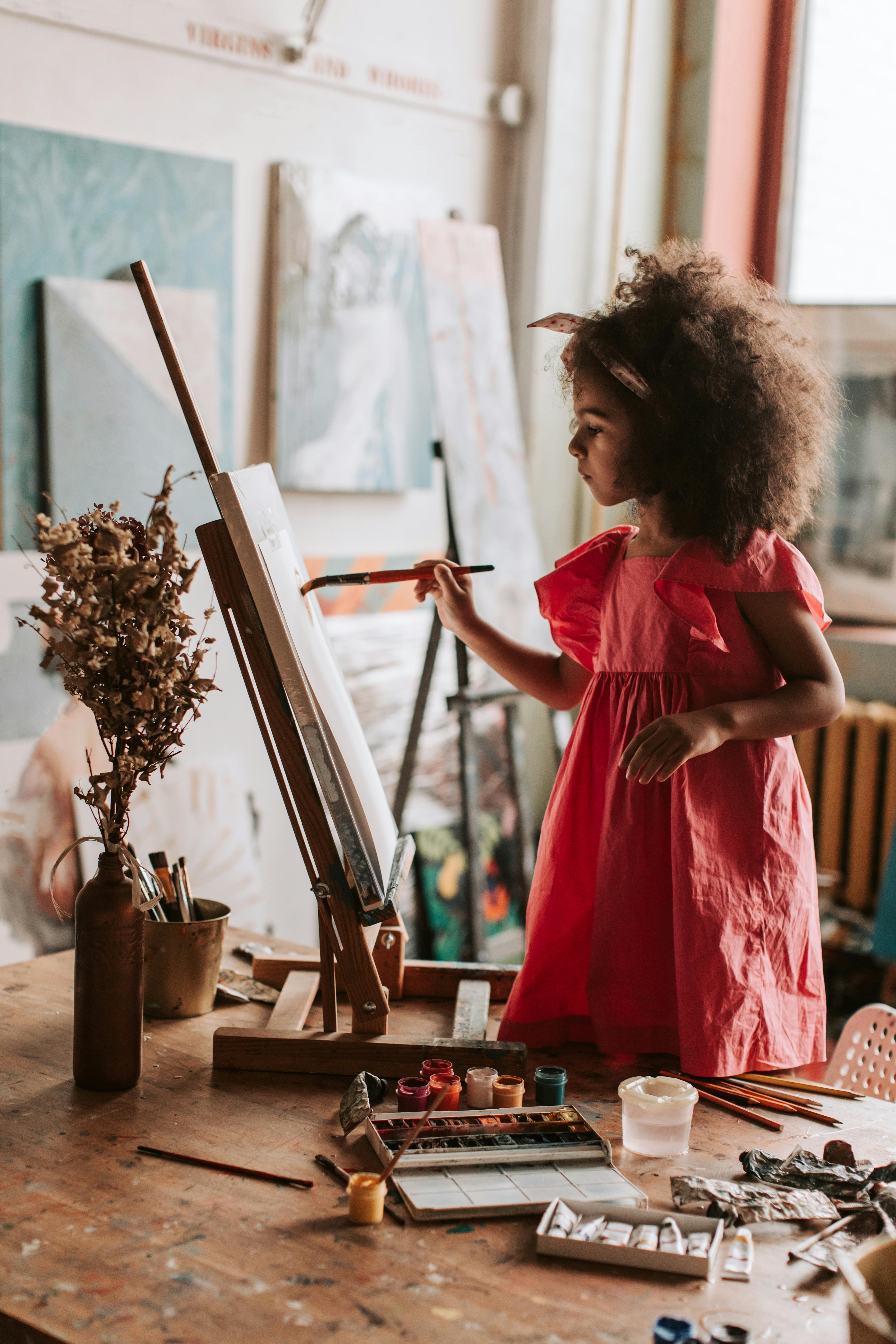 A young girl with curly hair painting on an easel in a cozy art studio, displaying creativity.