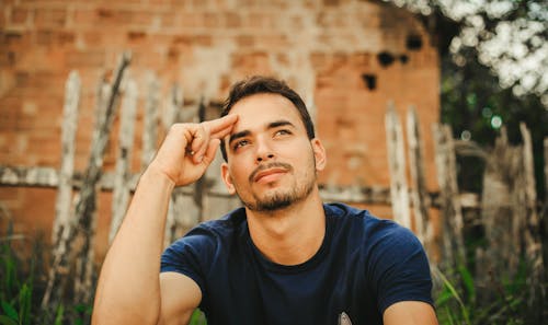 A Man in Blue Shirt Looking Up with His Hand on His Head