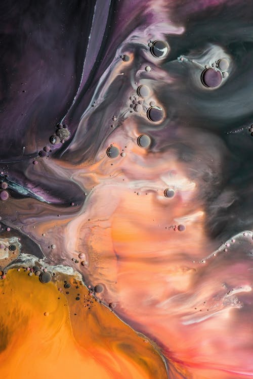 Abstract background of painting with pink and orange fluid acrylic paints creating stains on colorful artwork with dark purple patterns and bubbles