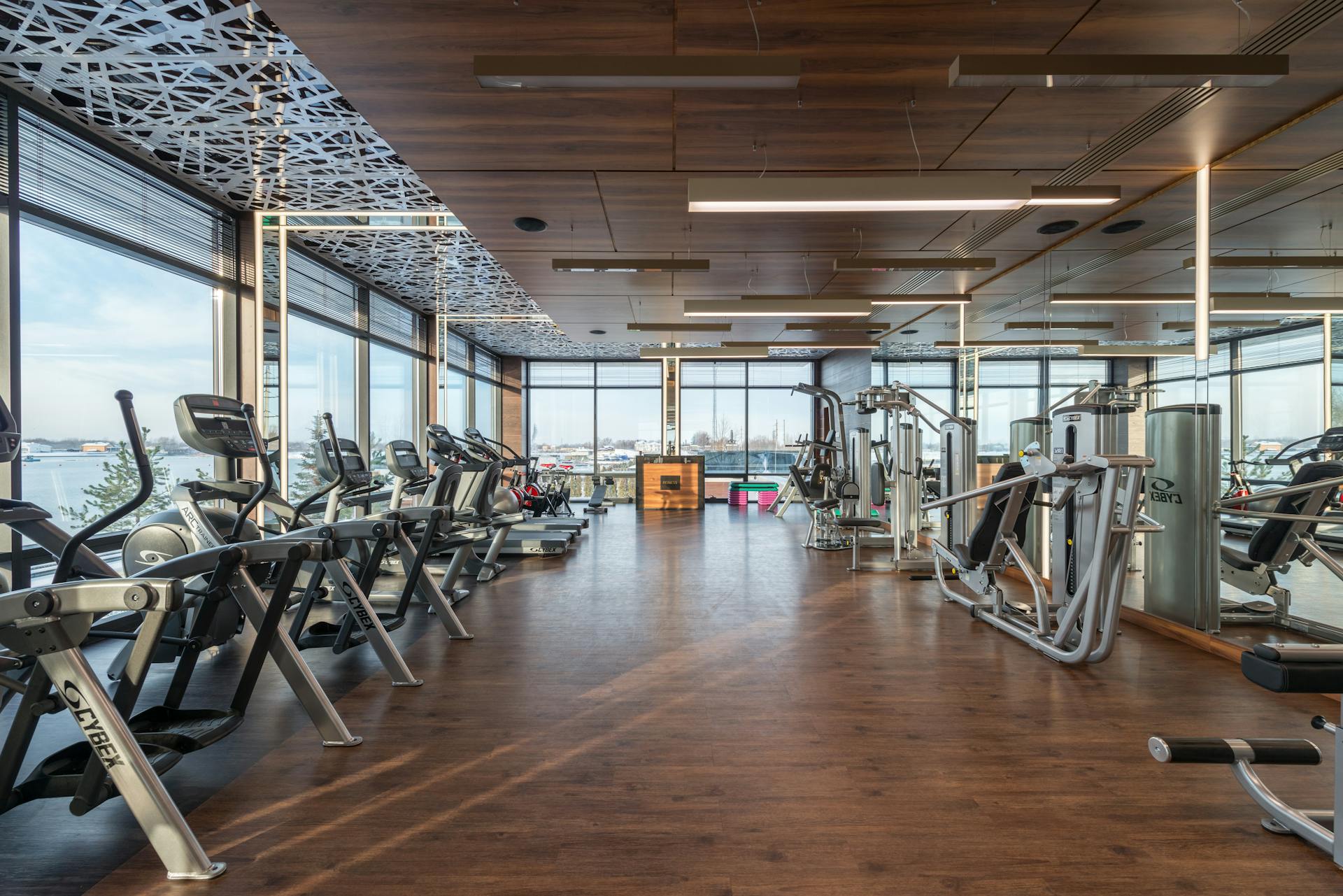 Interior of modern spacious fitness club with various sports machines and equipment placed on parquet floor near panoramic windows