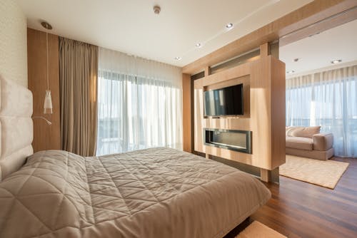 Interior of spacious apartment with cozy living room with soft bed separating from living room with sliding doors and wall with TV set in sunlight