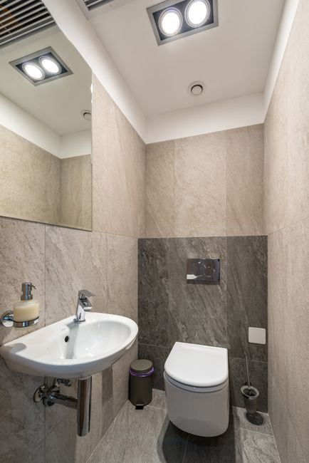 White ceramic sink and toilet bowl in modern bathroom with tiled walls and mirror