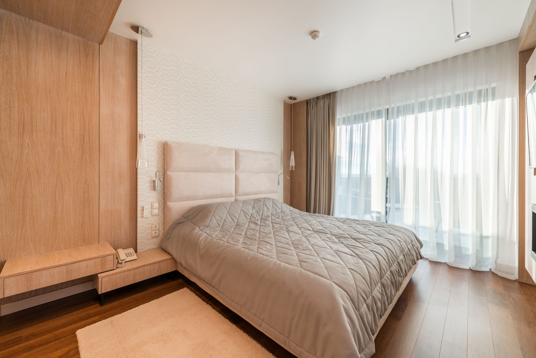 Comfortable bed with blanket placed at wall near window with curtains in modern stylish bedroom with wooden wardrobe with telephone