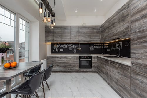 Chairs at table with fruits placed near window in modern spacious kitchen with gray cupboards and contemporary kitchenware in apartment