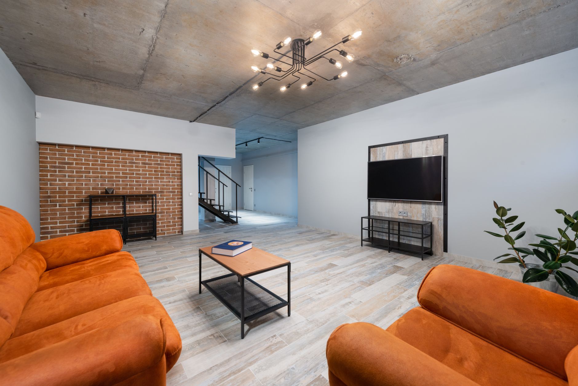 Soft orange sofa and armchair placed near coffee table in stylish living room with modern TV in apartment with stairway
