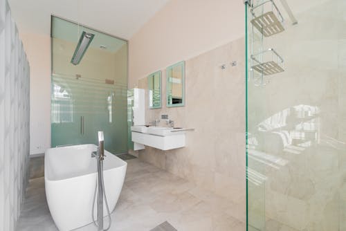 Light contemporary bathroom with white bath and glass shower cabin with beige tiles