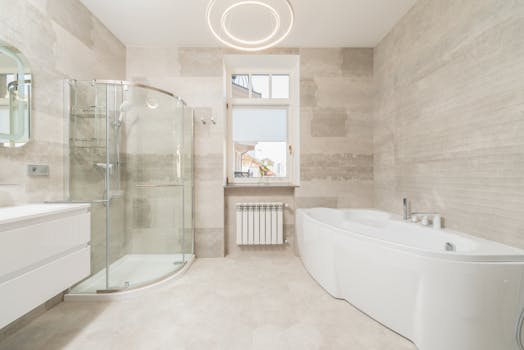 Modern spacious light bathroom with white bath and glass shower cabin near window