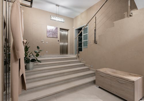 Spacious hallway of contemporary apartment with beige walls and wide stairway under glowing lamps