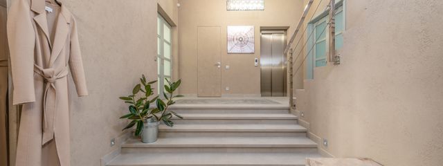 Modern lobby with elevator and wide staircase leading to hallway with bench and hanger shelf