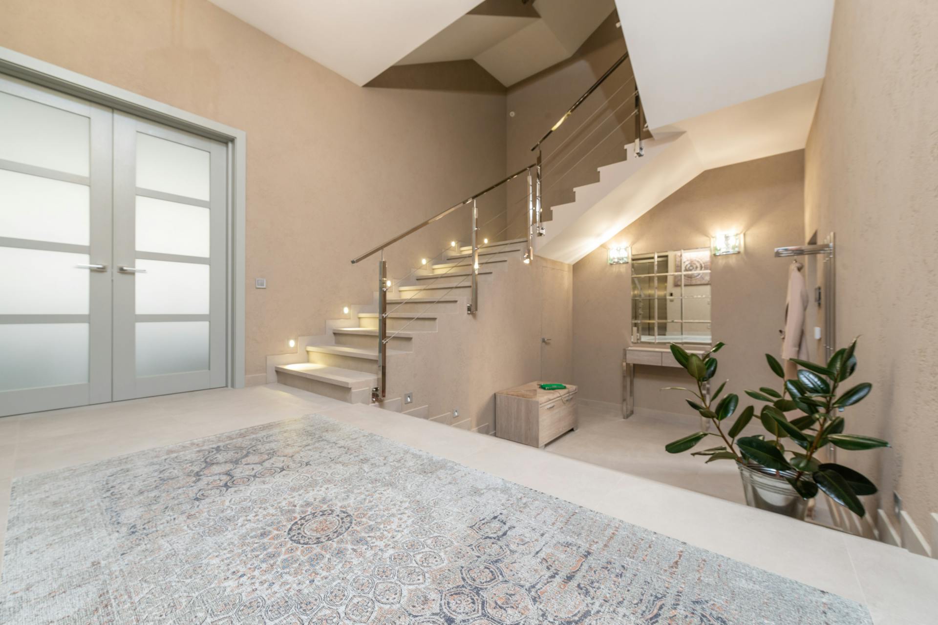 Interior of modern light lobby with beige walls and big glass doors with luminous stairway to second floor