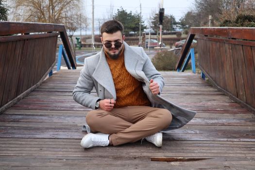Man in a Gray Coat Sitting on a Wooden Bridge