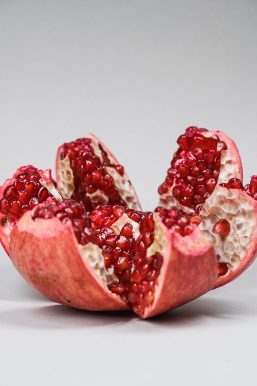 Free Detailed shot of a fresh, split pomegranate showcasing vibrant red seeds on a neutral background. Stock Photo