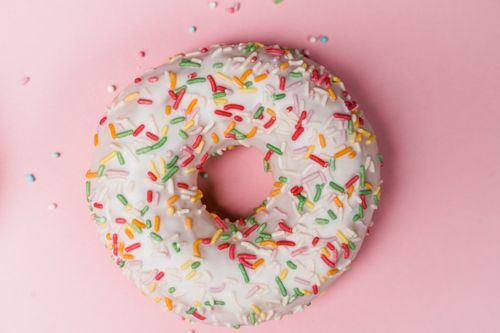 Free Top view of a sprinkled donut on a pastel pink surface, showcasing vibrant colors. Stock Photo